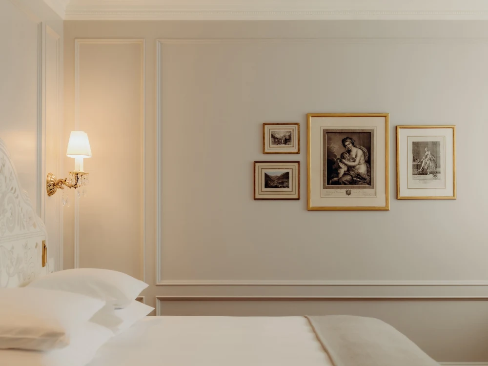 Deluxe Double Room, Village Side — bedroom with white panelling, wall sconce and framed prints